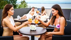 A group of people seated on outdoor wicker furniture, holding drinks, with a view of the sea in the background. - Hotel Thermal ŠÍRAVA (Kaluža)