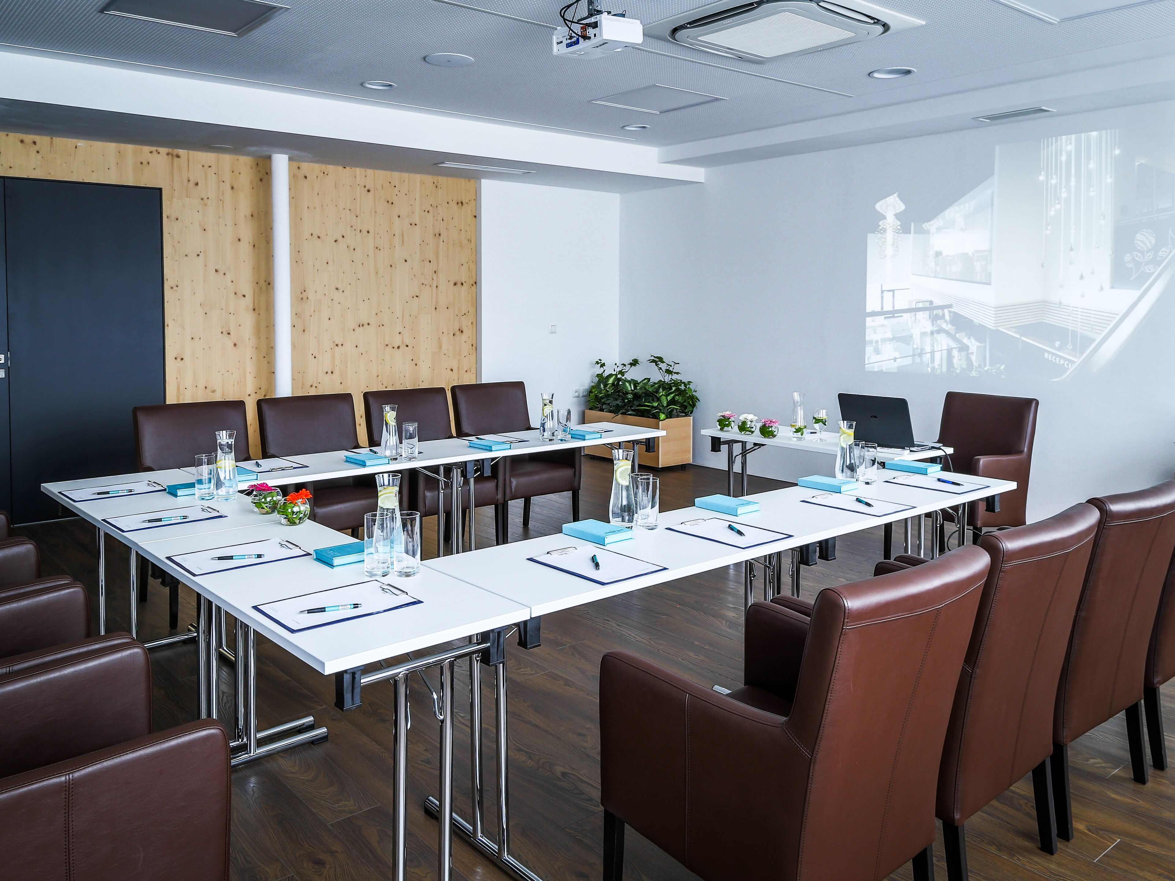 Ein moderner Konferenzraum mit einem langen Tisch, braunen Ledersesseln und einer Projektionsleinwand.