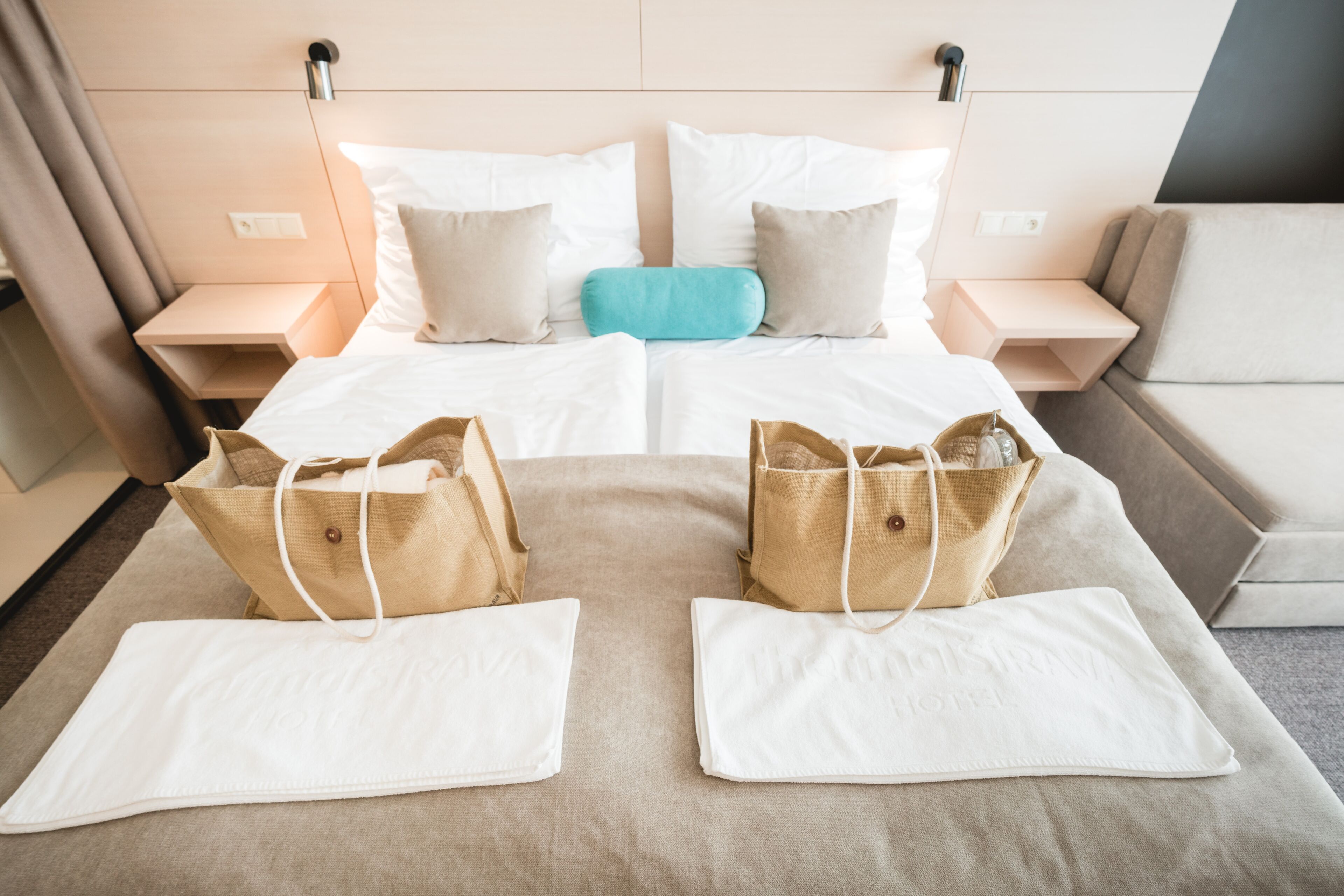 Una habitación de hotel con una cama, dos mesitas de noche, un sofá y dos maletas sobre la cama.