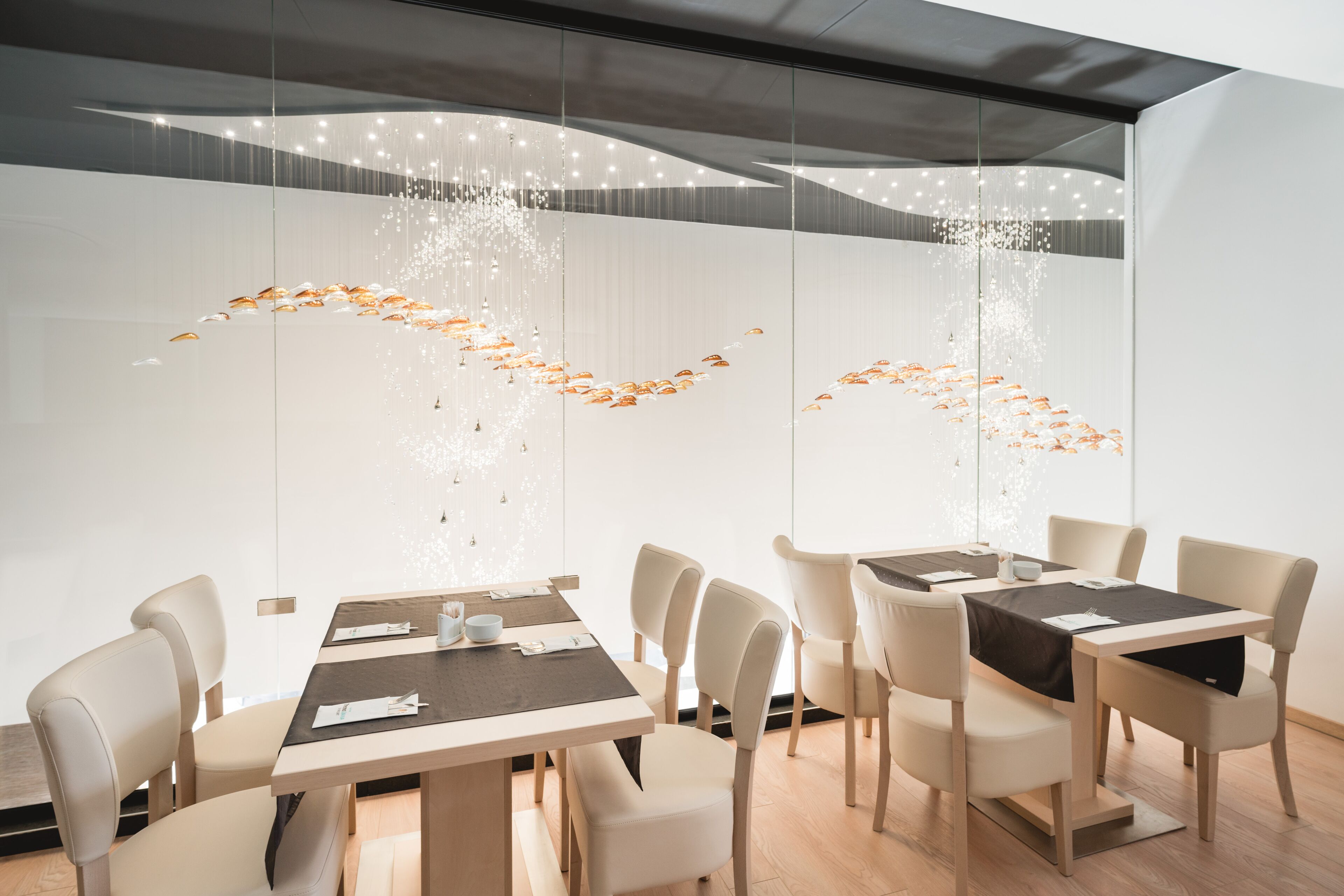 A modern dining area with a long table, several chairs, and a decorative light installation on the wall.
