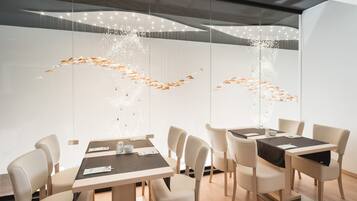 A modern dining area with a long table, several chairs, and a decorative light installation on the wall.
