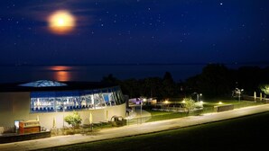 A modern building with a glass facade, outdoor seating area, and a view of the water. - Hotel Thermal ŠÍRAVA (Kaluža)