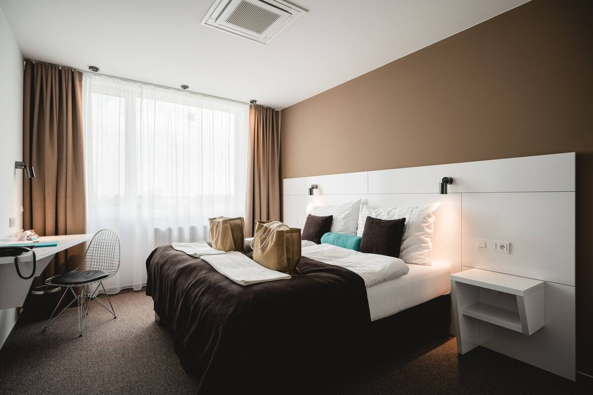 A hotel room with a bed, a desk, a chair, and a nightstand.