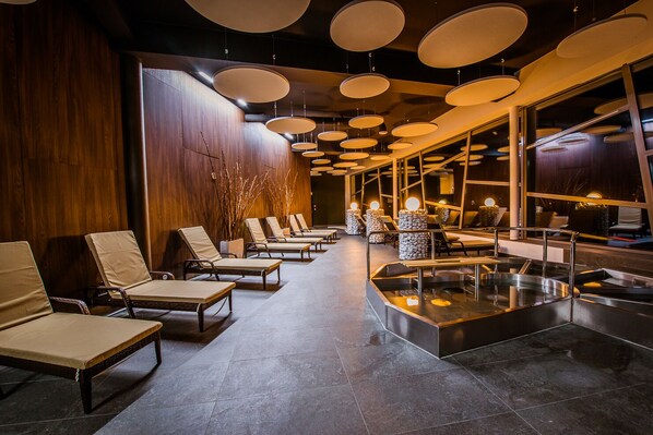 A modern spa area with lounge chairs, a heated stone bath, and a wooden wall.