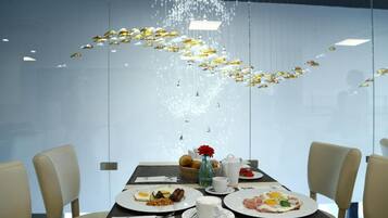 Een eettafel met ontbijtbestek, een vaas met een rode bloem en een hanglamp.