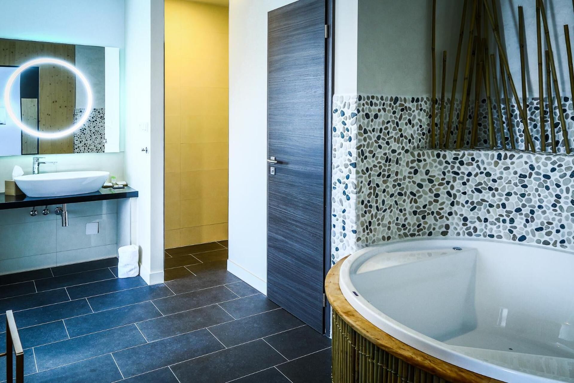 Un baño moderno con una bañera grande, un lavamanos con espejo y una puerta que da a otra habitación.