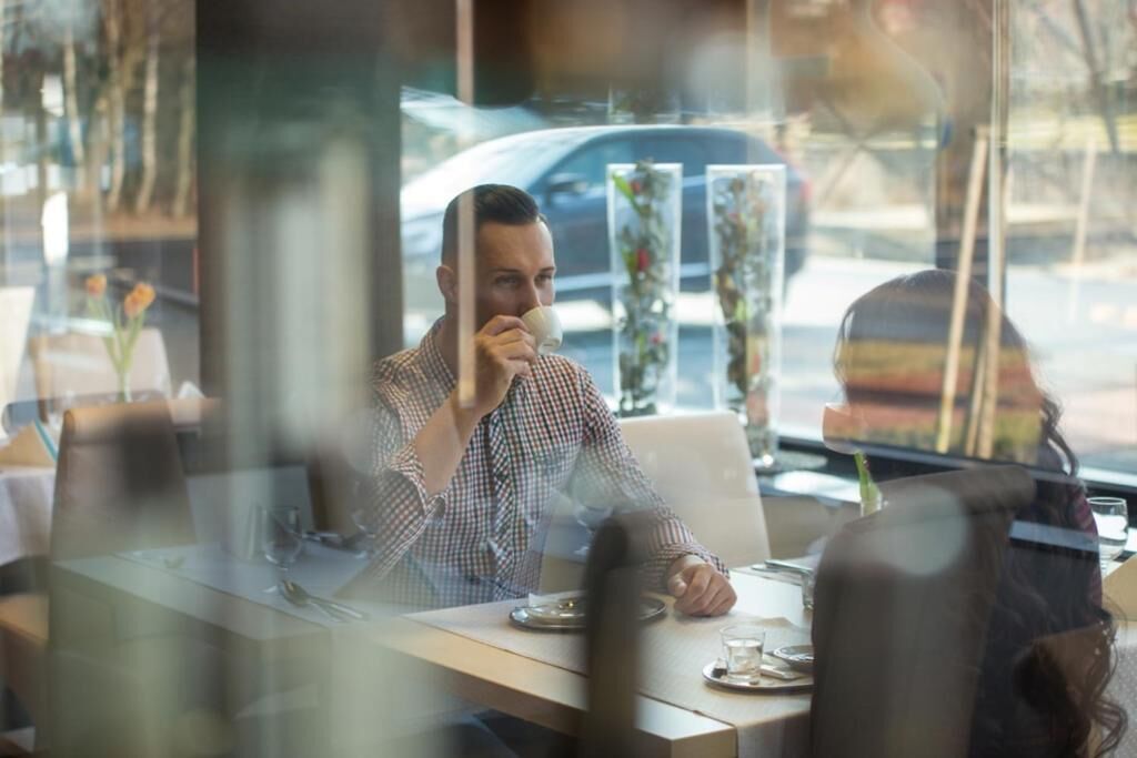 A person sitting at a table in a restaurant with a window view.