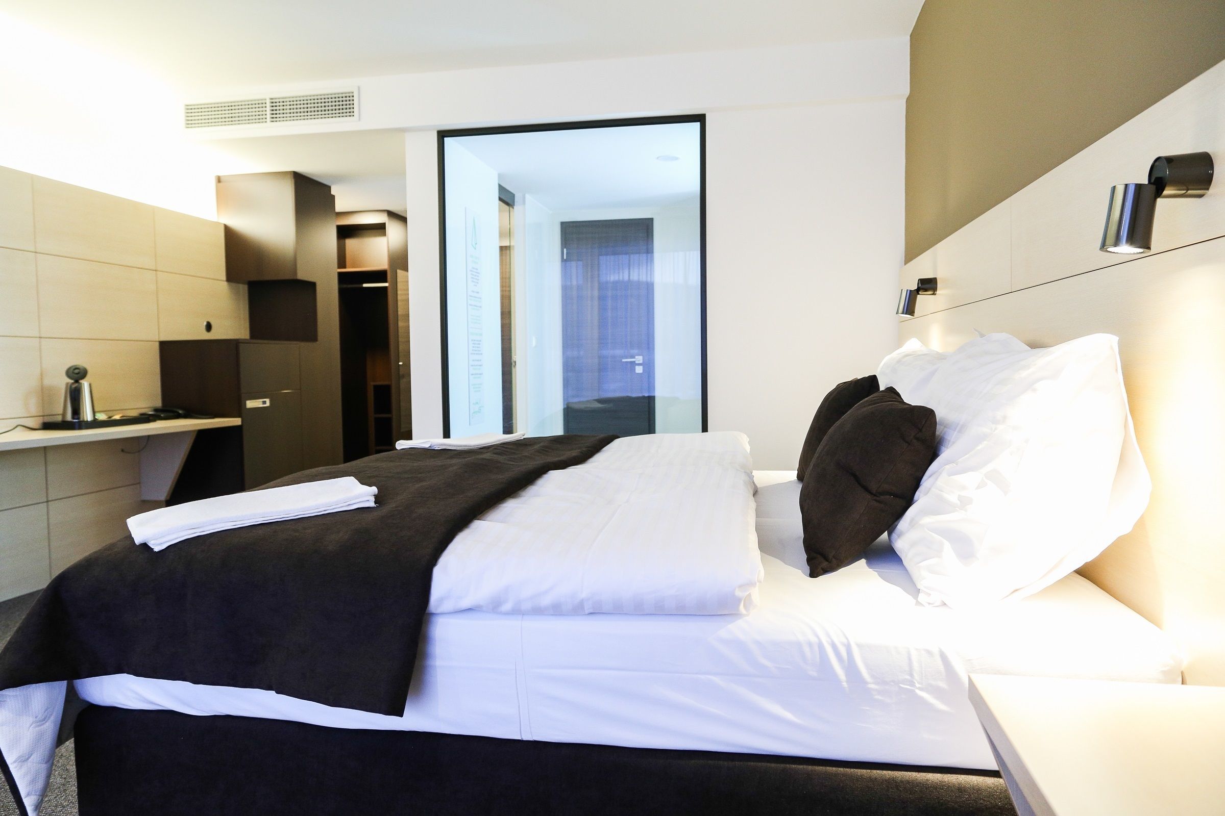 Moderni hotellihuone, jossa on siististi pedattu sänky, yöpöytä ja suuri peili.