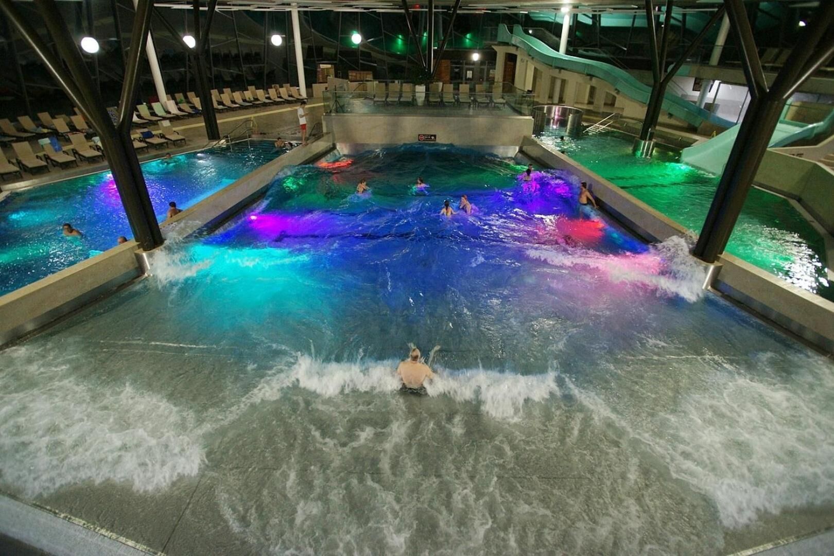Un parque acuático interior grande con múltiples piscinas y toboganes.