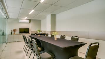 A conference room with a long table, chairs, a flat-screen TV, and potted plants.
