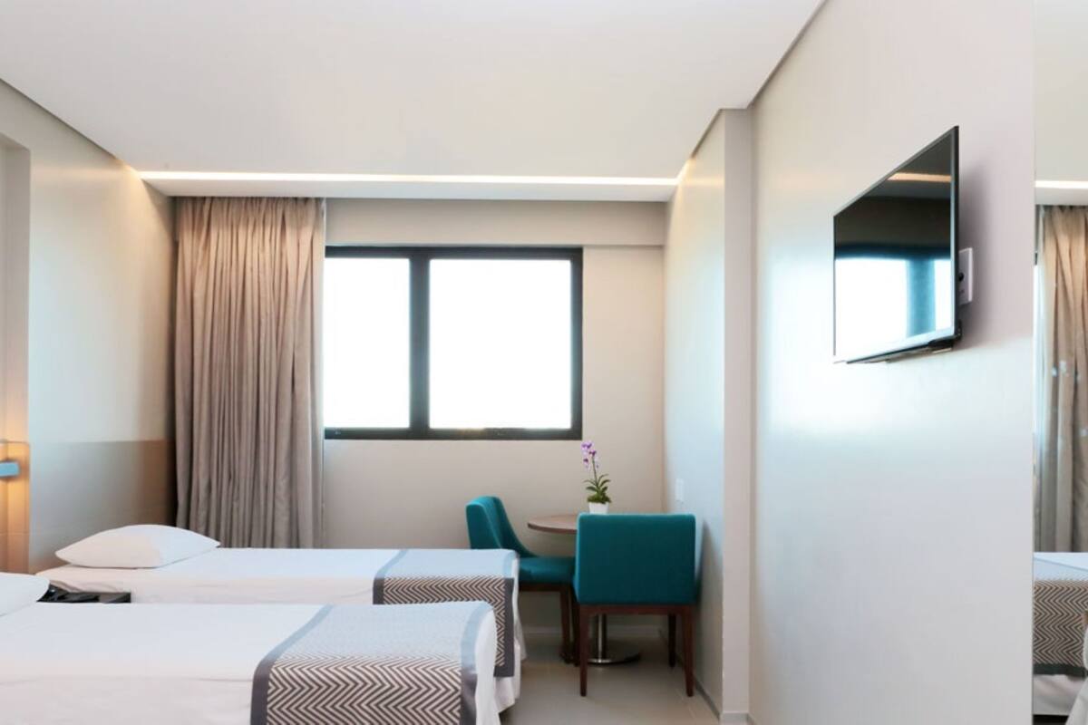 A hotel room with two beds, a desk, a chair, a TV, and a window with curtains.