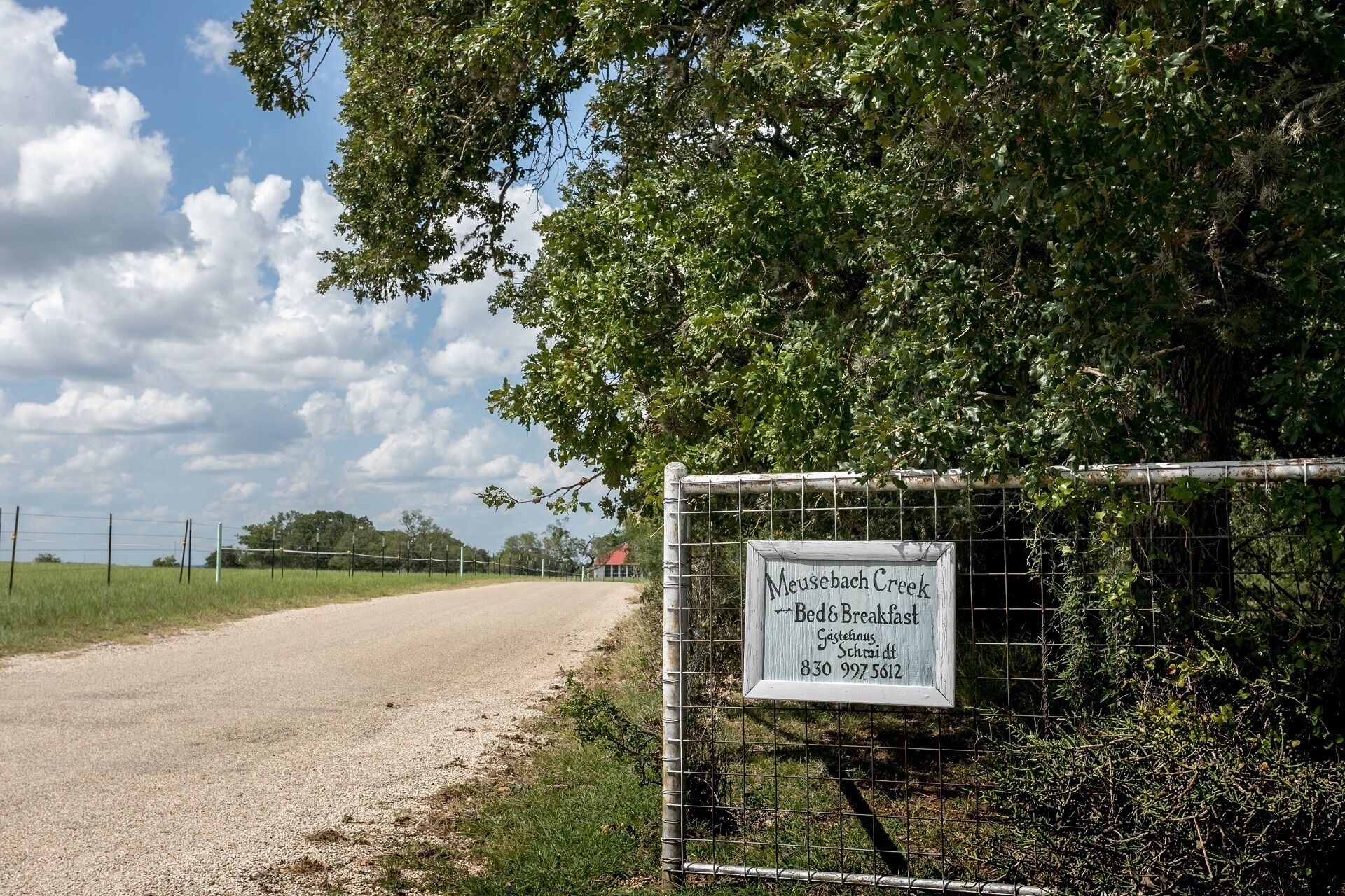 A sign for Meusebach Creek Bed & Breakfast, indicating a rustic, fenced property with a gravel road leading to it.