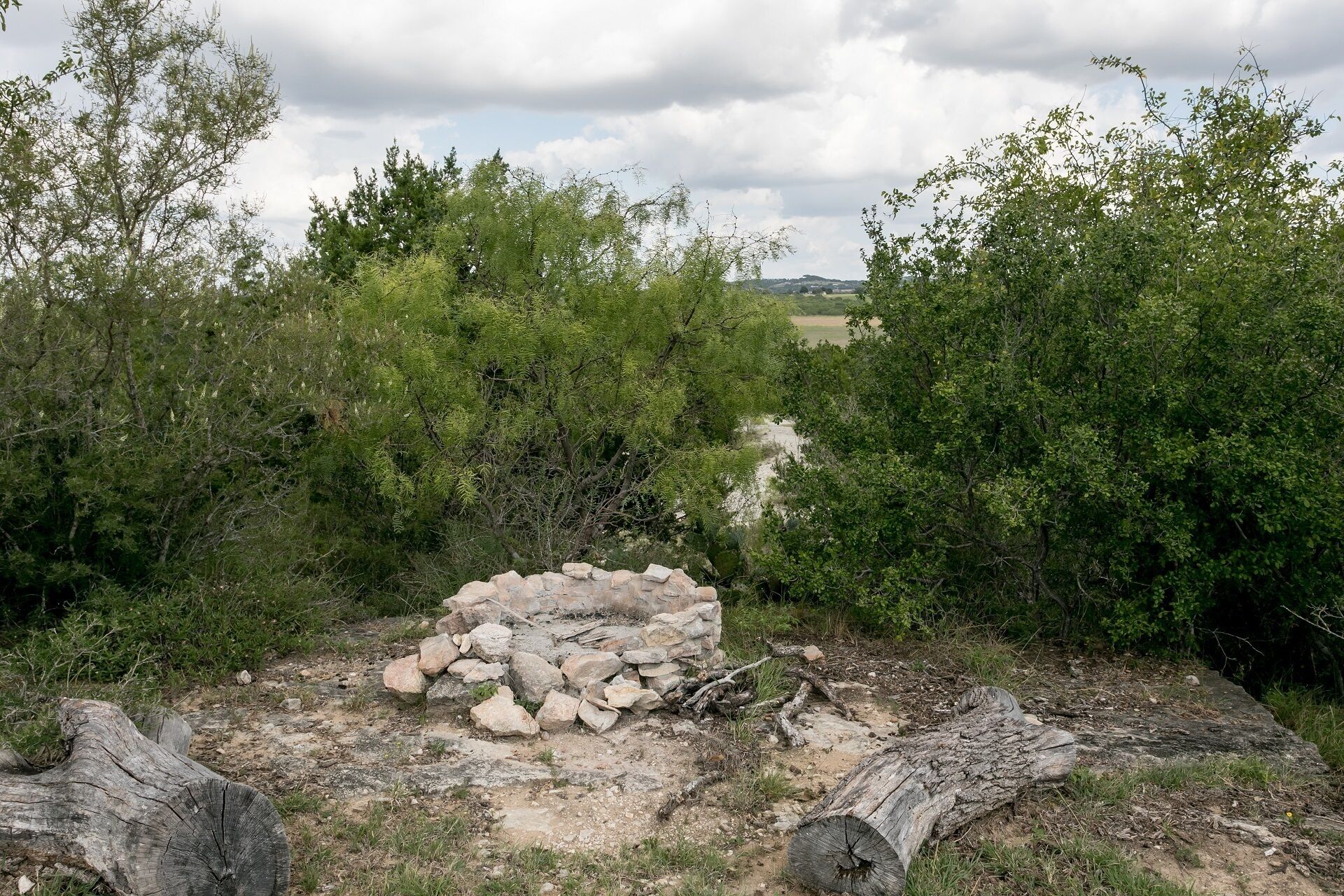 Paisaje natural con una estructura de piedra en primer plano, rodeada de densa vegetación y árboles.