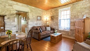 Una habitación acogedora con pared de piedra, techo de madera, un sofá de cuero marrón, una mesa de madera y una silla.