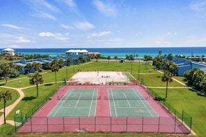 A tennis court with a surrounding fence, palm trees, and a view of the ocean. - Unit 14, Peaceful Palms, 2.5 Bedroom Beach Condo (Panama City Beach)