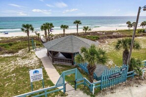 A beachside building with a covered patio, a gated entrance, and a view of the ocean. - Unit 14, Peaceful Palms, 2.5 Bedroom Beach Condo (Panama City Beach)