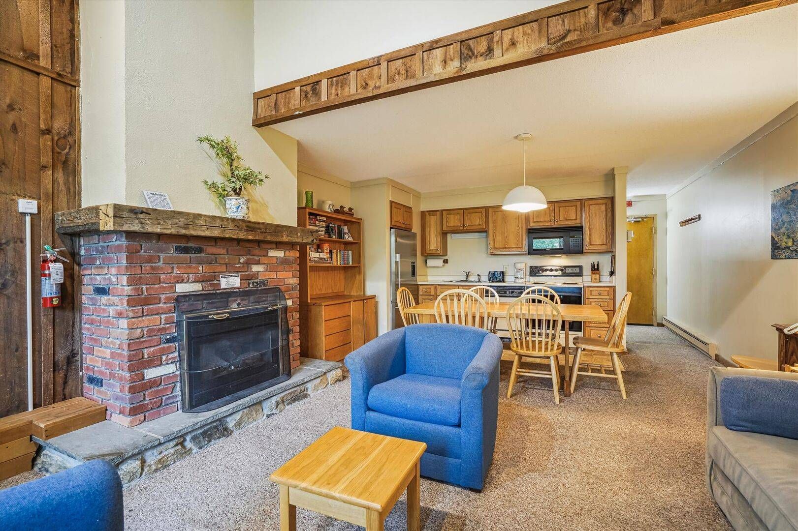 A cozy living room with a fireplace, a dining area with wooden chairs, and a kitchen with wooden cabinets.
