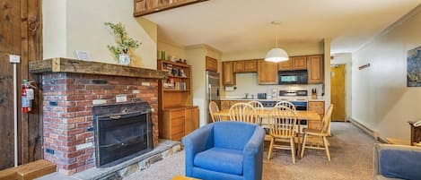 A cozy living room with a fireplace, a dining area with wooden chairs, and a kitchen with wooden cabinets.