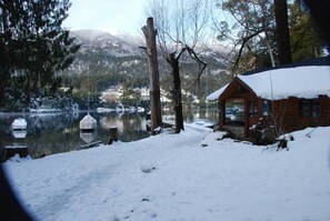 A cabin by a lake with snow on the ground and trees. - Hosteria Lekun Lekun (Villa La Angostura)