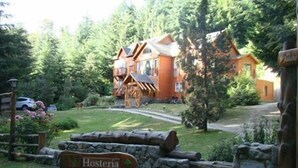 Tunnelmallinen, maalaishenkinen mökki, jonka luokse johtaa kivipolku. Polun päässä on puinen rakennus. Kyltissä näkyy opasteet kohteisiin nimeltä ”Hosteria” ja ”Lekun Lekun”.
