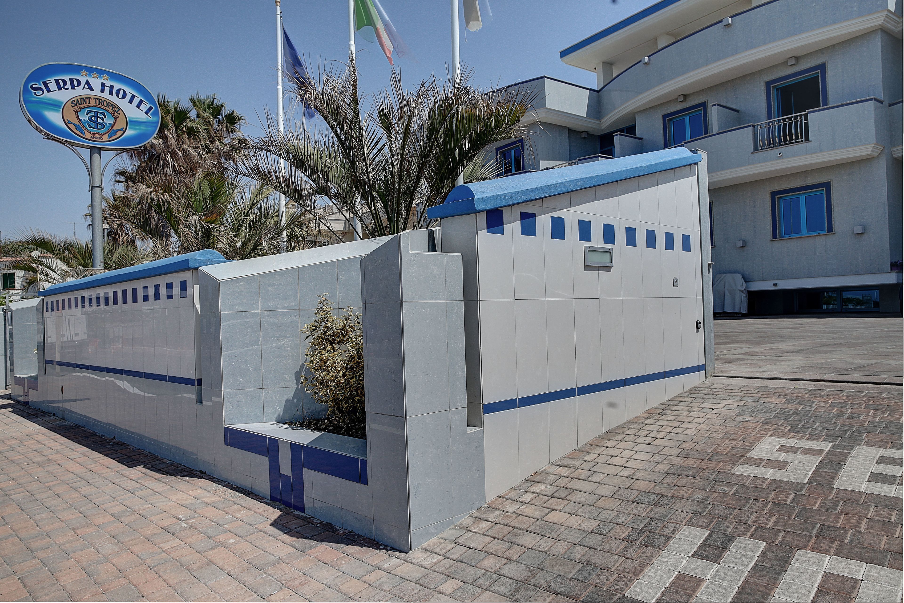 Entrada de hotel com placa, área murada e edifício com varandas.