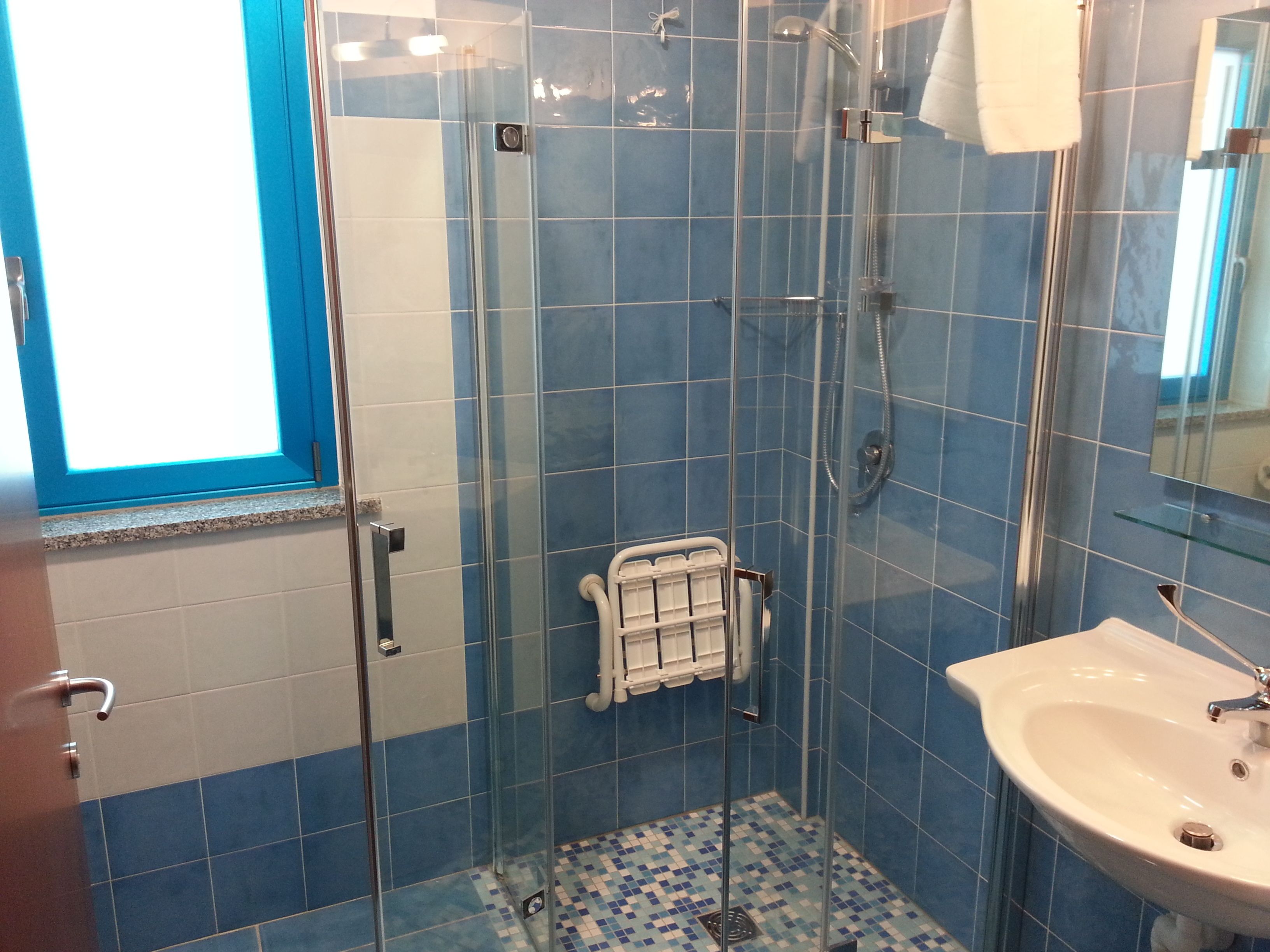 Un baño con ducha de vidrio, un lavabo blanco y paredes con azulejos azules.