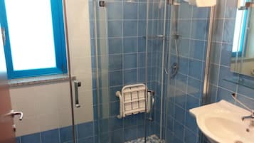 Een badkamer met een douchecabine van glas, een wit wastafelmeubel en blauwe betegelde wanden.