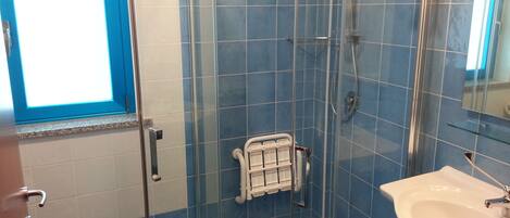 Un baño con ducha de vidrio, un lavabo blanco y paredes con azulejos azules.
