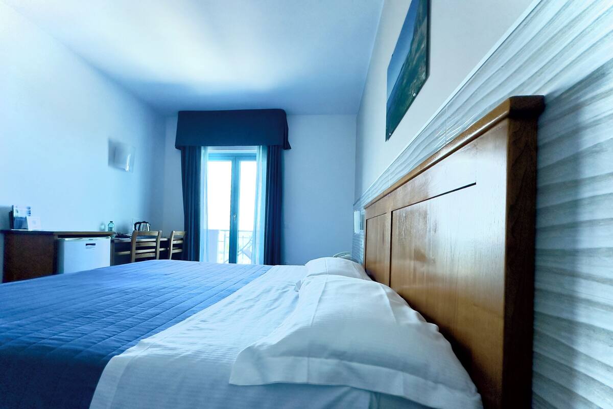 A hotel room with a bed, a desk, a chair, and a window with curtains.