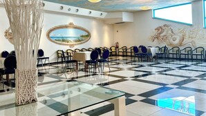 A spacious room with a checkered floor, round tables, and chairs, a decorative vase, and a mural on the wall. - Serpa Hotel Anzio (Anzio)