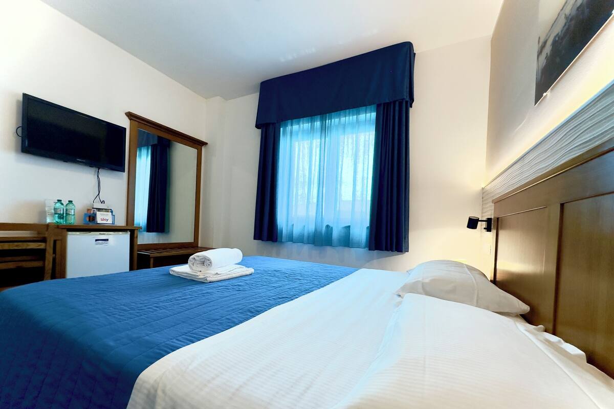 A hotel room with a bed, a desk, a television, and a window with curtains.