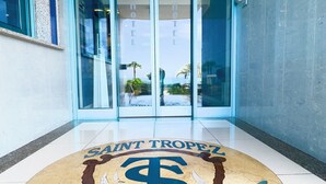 A hotel entrance with a glass door, a sign reading "SAINT TROPEZ ANZIO", and a circular emblem featuring a dollar sign and dolphins. - Serpa Hotel Anzio (Anzio)