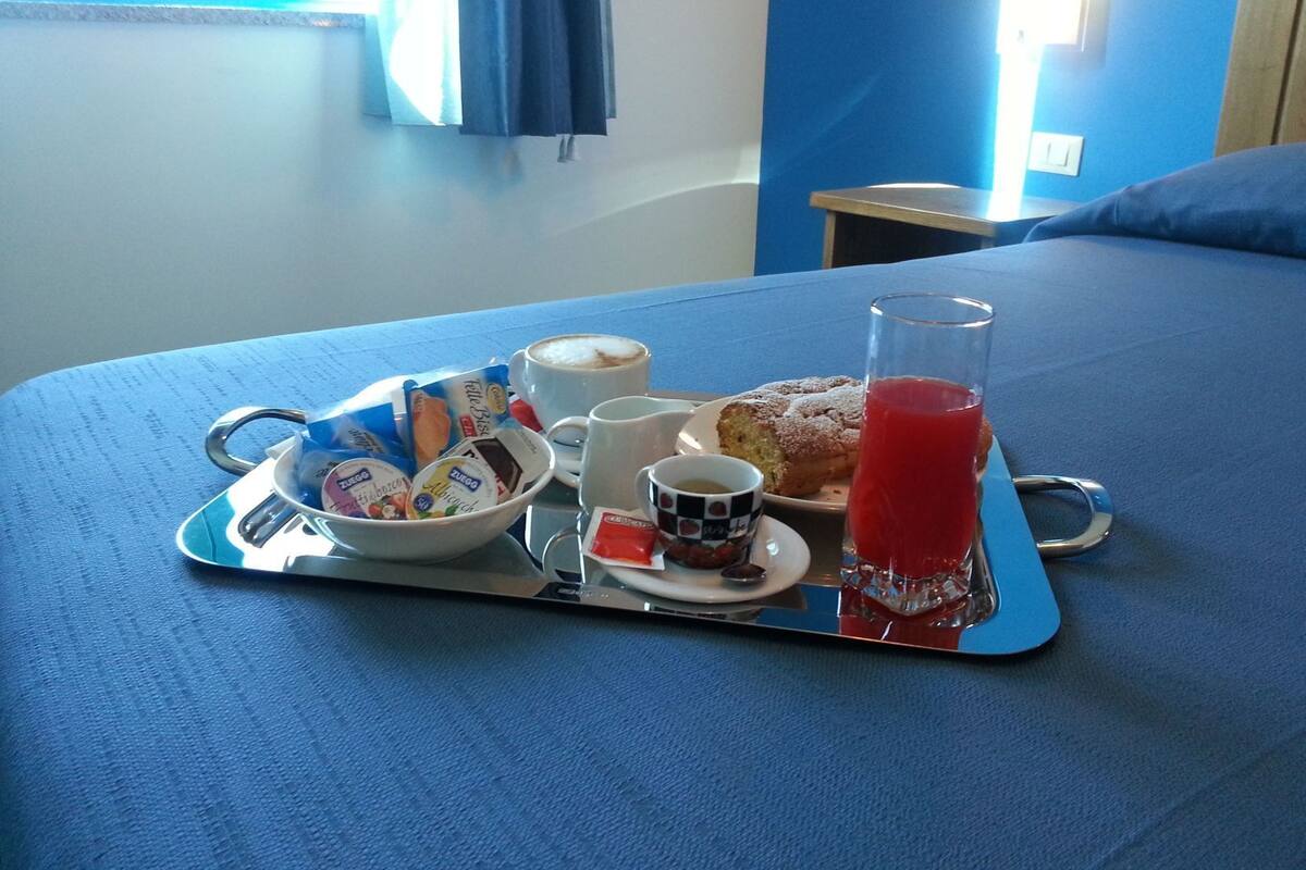 A breakfast tray on a bed with a cup of coffee, a pastry, a glass of juice, and a bowl of yogurt.