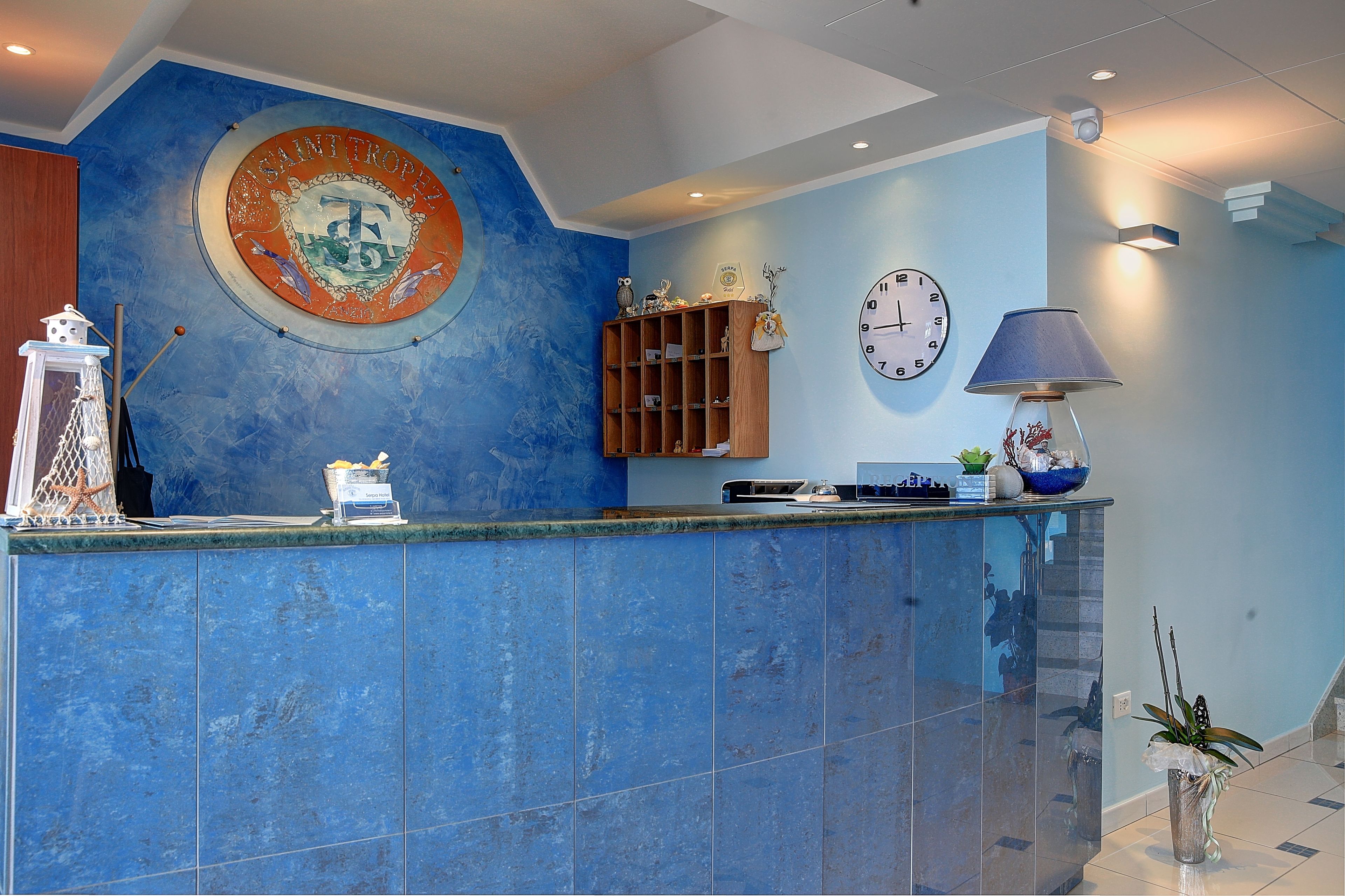 A reception area with a blue tiled counter, a clock, and a wall-mounted emblem.