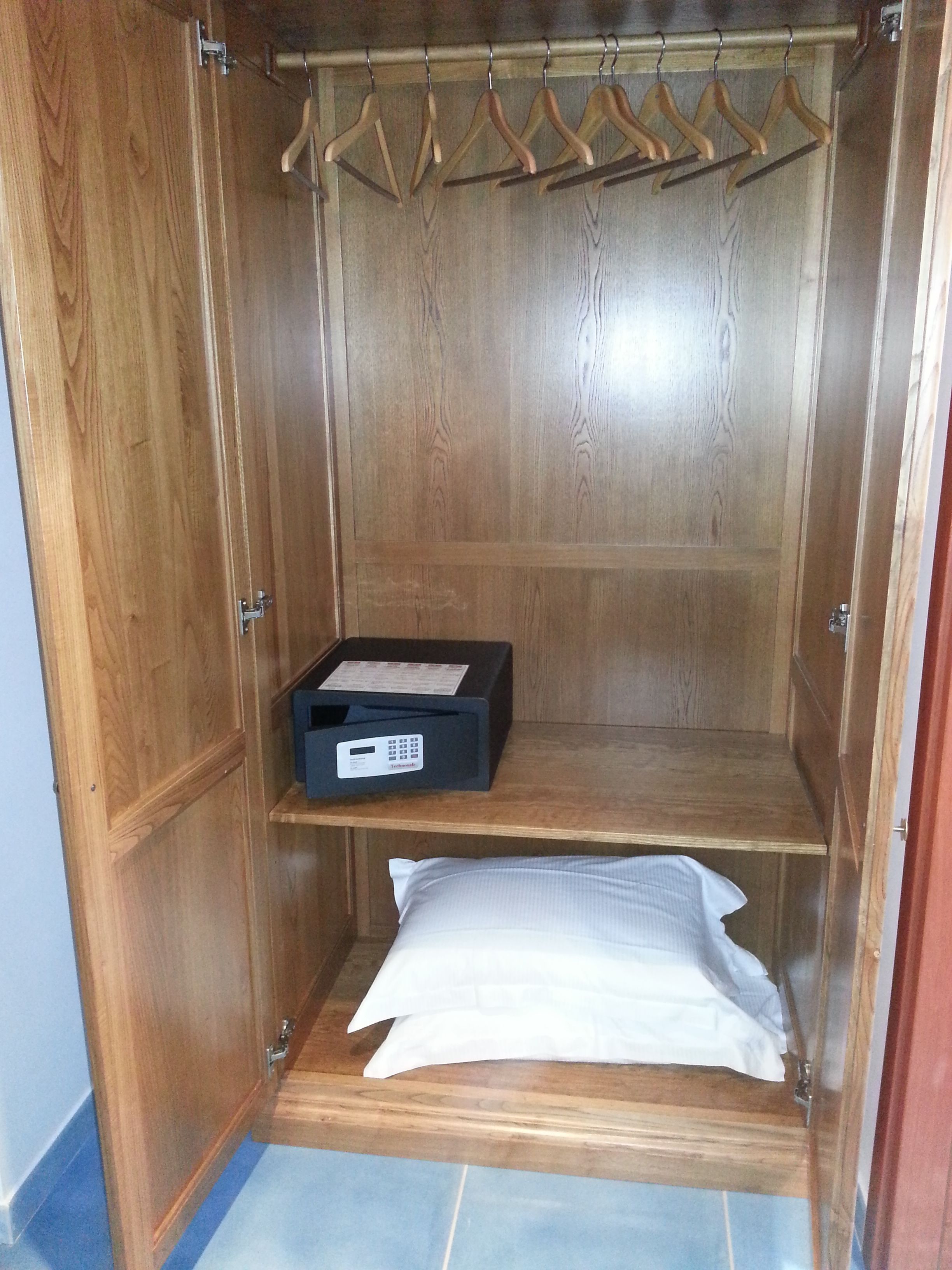 A wooden closet with a hanging rod, a shelf with a box, and a folded white item on the floor.
