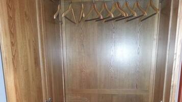 A wooden closet with a hanging rod, a shelf with a box, and a folded white item on the floor.