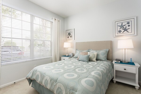 Un dormitorio ordenado con una cama, dos mesitas de noche y una ventana con persianas.