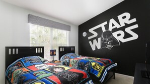 A bedroom with Star Wars themed bedding, a black wall with Star Wars logo, and a window with blinds.