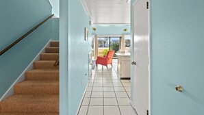 A hallway with a carpeted staircase, a chair, and a door leading to an outdoor area.