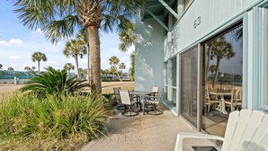 An outdoor patio with a table and chairs, palm trees, and a building with a large window.