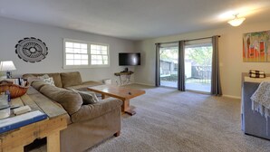 Ein Wohnzimmer mit Sofa, Couchtisch und Fernseher. Ein Fenster und eine Tür führen nach draußen.