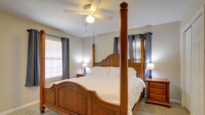 Ein Bett mit Baldachin, ein hölzernes Kopfteil, zwei Nachttische mit Lampen und ein Deckenventilator.