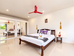 Quarto espaçoso com uma cama grande, um ventilador de teto vermelho e vista para área externa por uma porta de vidro.