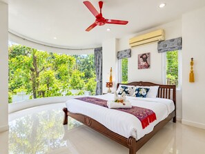 A bedroom with a large bed, a ceiling fan, and a view of greenery outside. - Villa Nap Dau Crown Private pool villa for Family and Friends (ต.ฉลอง)