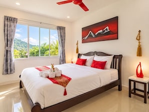 Habitación de hotel con una cama grande, ventilador de techo, un cuadro y vistas a zonas verdes.