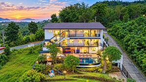 A multi-story hotel with a swimming pool, surrounded by lush greenery and a view of the sunset. - Villa Nap Dau Crown Private pool villa for Family and Friends (ต.ฉลอง)