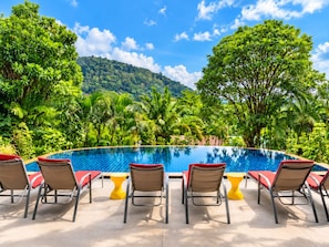 Una piscina con sillones de descanso y vistas a un paisaje verde exuberante.
