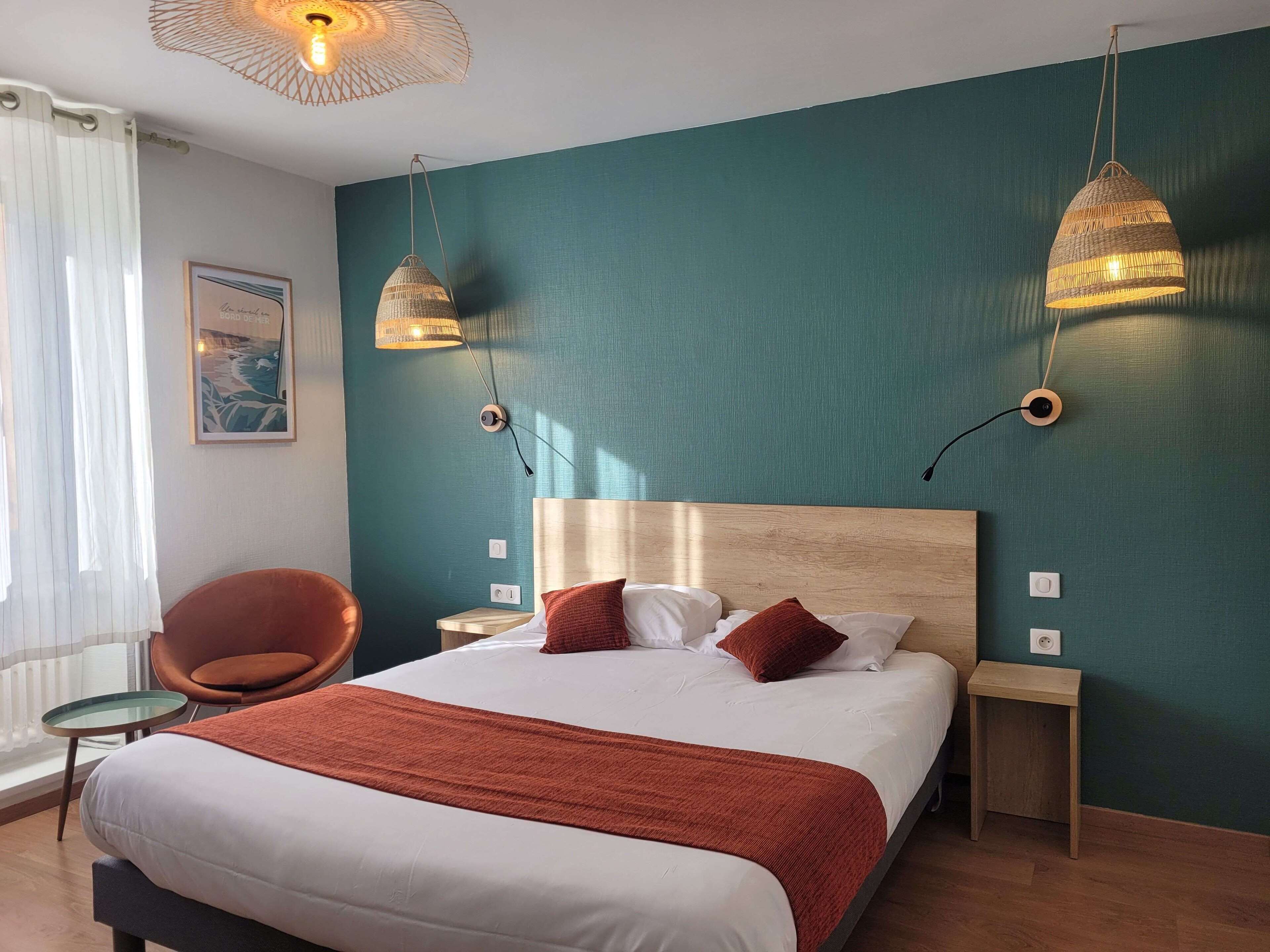 Una habitación de hotel con una cama grande, dos mesitas de noche, una silla y dos lámparas colgantes.