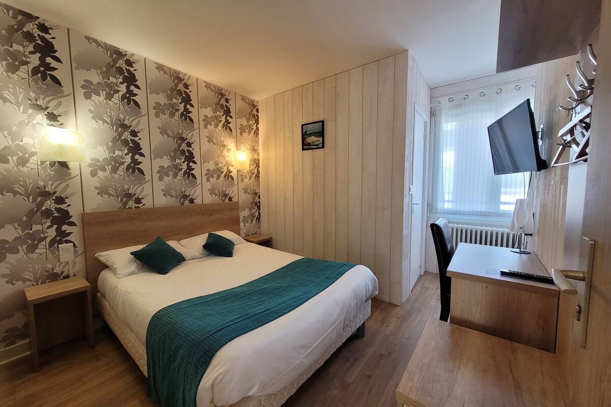 A bedroom with a wooden bed, a desk with a chair, a TV, and a radiator.