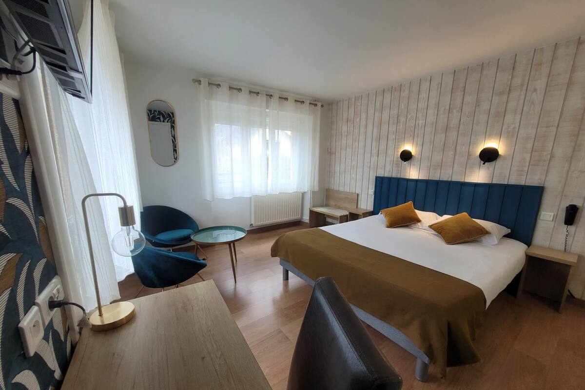 A hotel room with a bed, a desk, a chair, a small table, and a window with curtains.